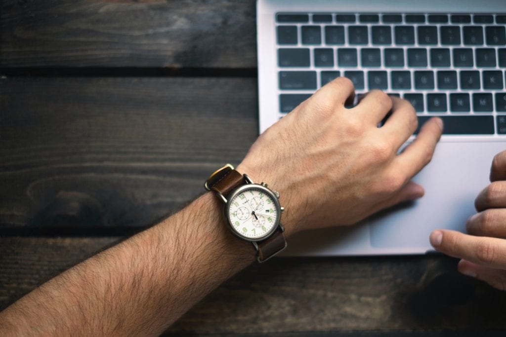 Man wearing a watch with his arm on a laptop