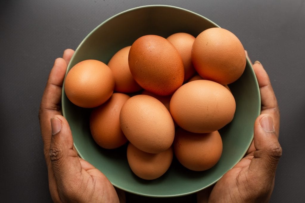 hands holding a bowl of brown eggs