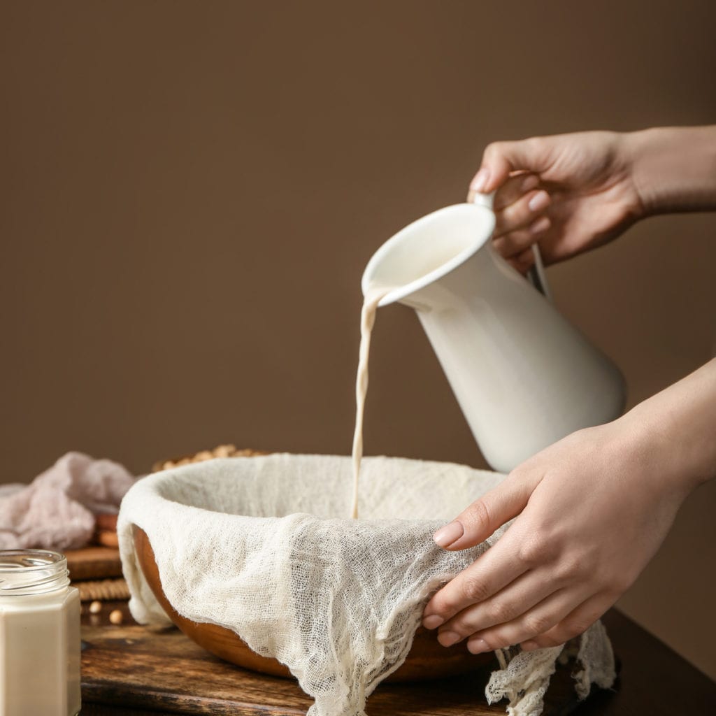 soy milk being poured into a bowl with a cheesecloth