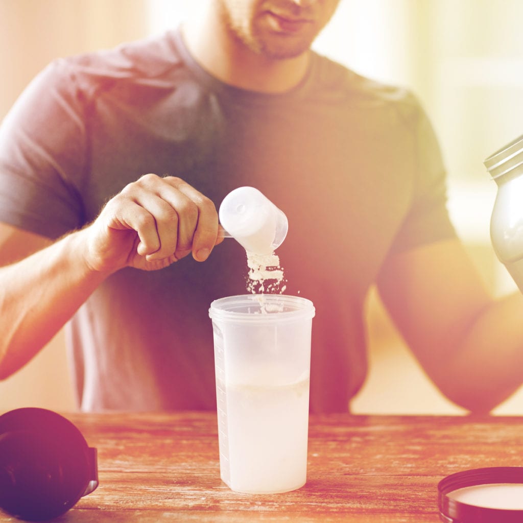 man pouring creatine into his protein shake bottle