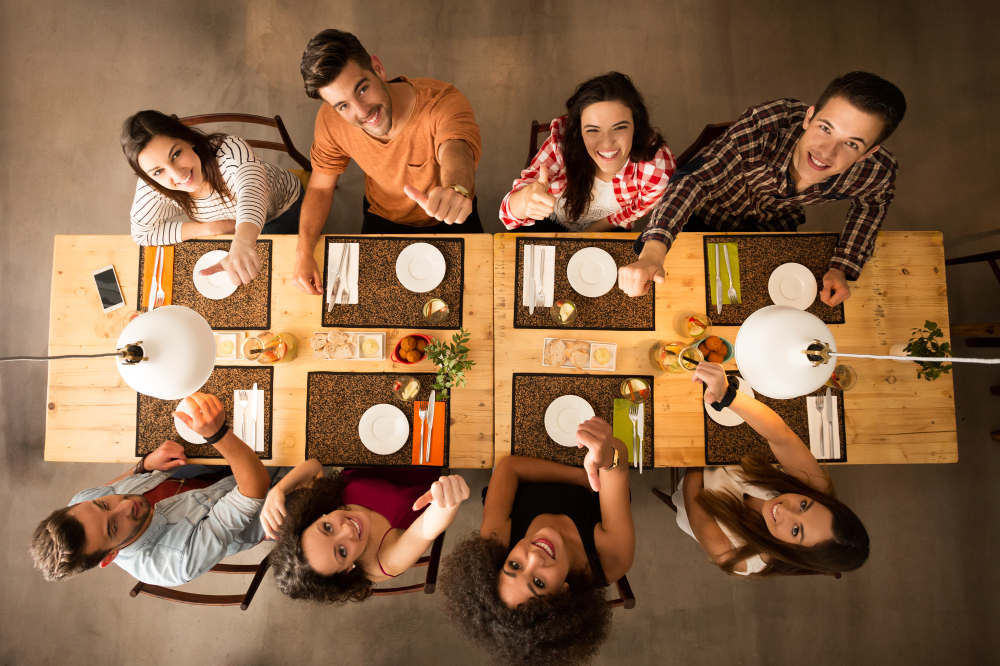 People gathered around a table with place settings, aerial view, looking up and giving thumbs up while smiling