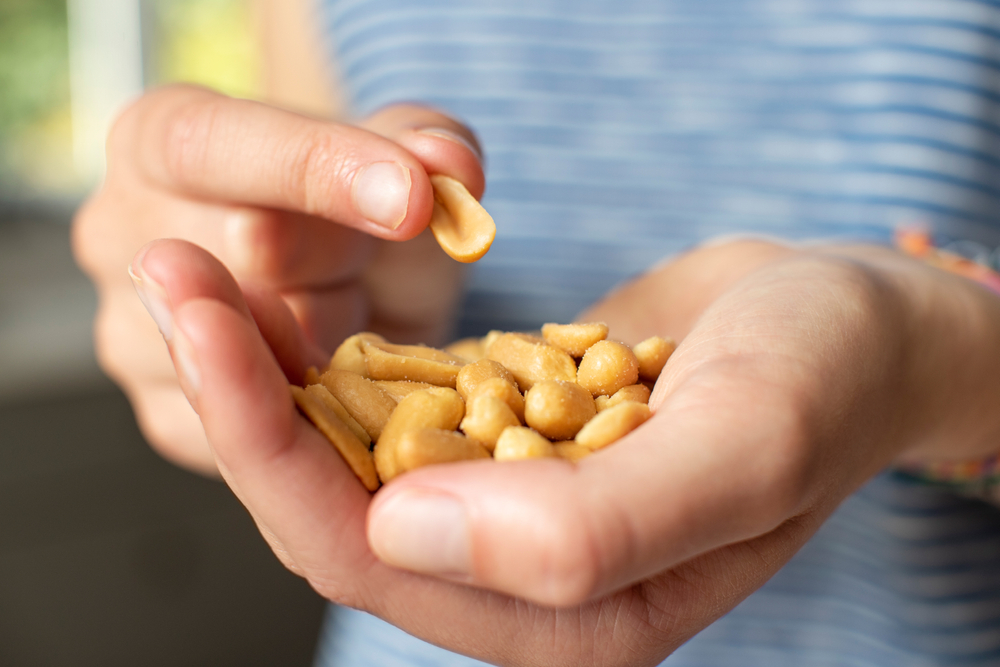 Close up of a person cupping a handful of shelled peanuts, holding one up, about to eat it.