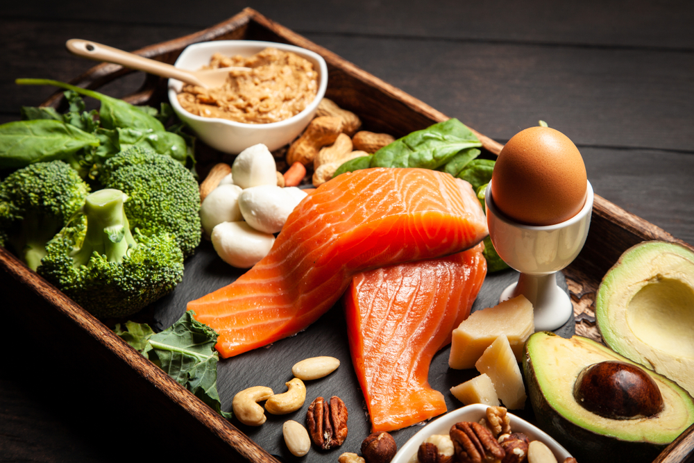 A tray of high-fat, low-carb Keto foods like salmon, broccoli, nuts, eggs, mozzarella, and avocado.