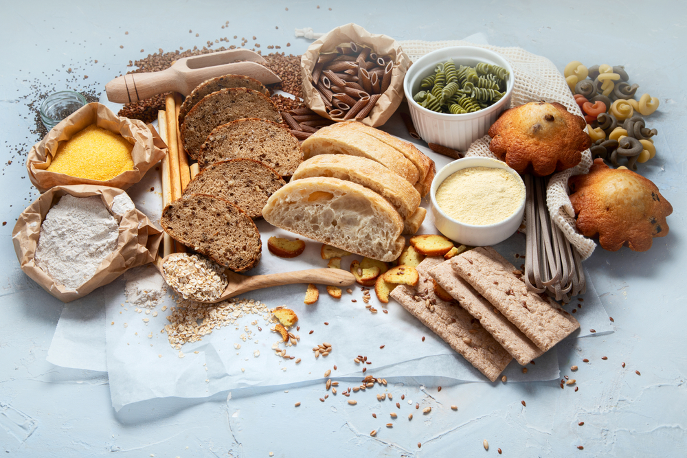 High carb non-Keto foods on a white background, sitting on white parchment paper: various breads, grains, crackers, bagged pastas, muffins, and oats. 