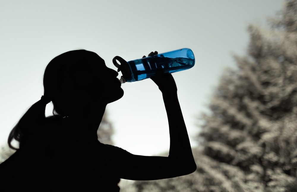Silhouette of a woman, outdoors, drinking from her water bottle.