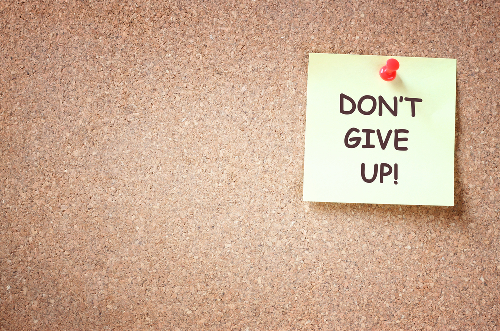 a sticky note that says "don't give up!" tacked onto a corkboard
