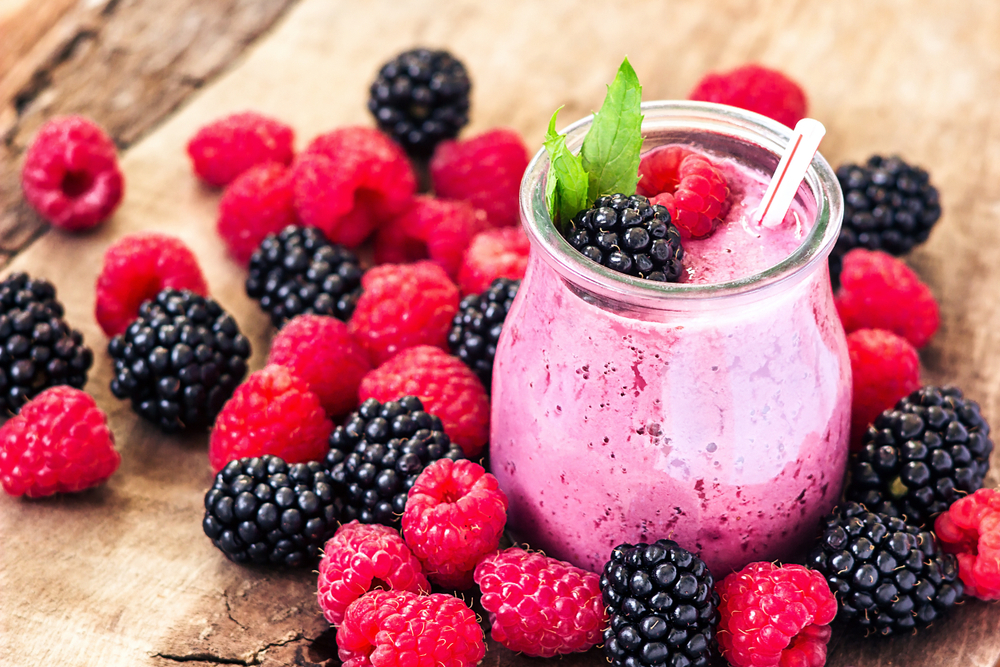 Small glass of a berry smoothie surrounded by a pile of fresh raspberries and blackberries