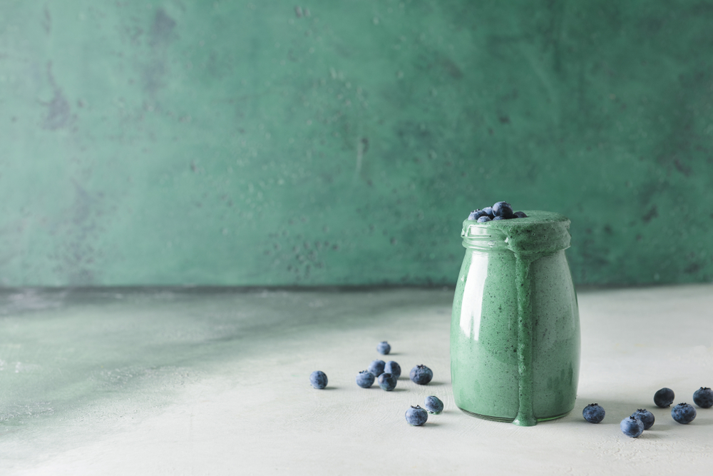 a jar of blue smoothie topped with blueberries on a blue and white background